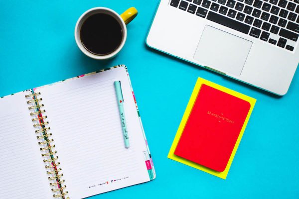 notebook, computer, coffee, and planner on blue desk to make your music website