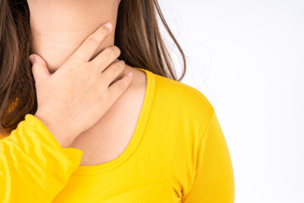 woman in bright yellow top touching throat like she is sick