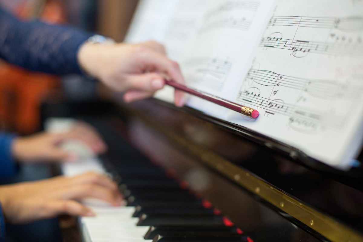 private music teacher in the music industry instructing piano student and pointing to sheet music with pencil