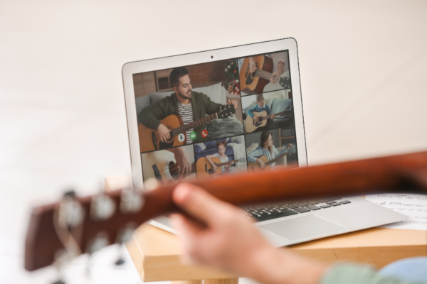 online music teacher teaching a group guitar class in front of a laptop
