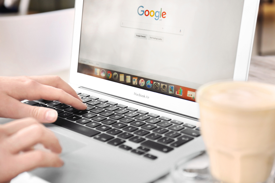 person with a MacBook Air open to google search with a light coffee in a glass cup