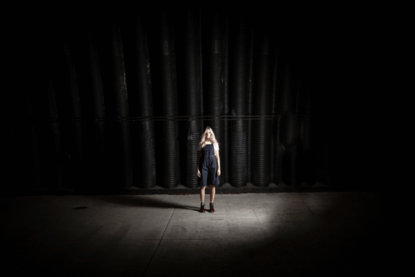 a woman standing alone in a spotlight in front of a black curtain