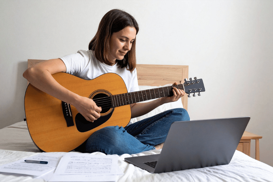 woman sitting on a bed learning to play guitar with the best music learning app