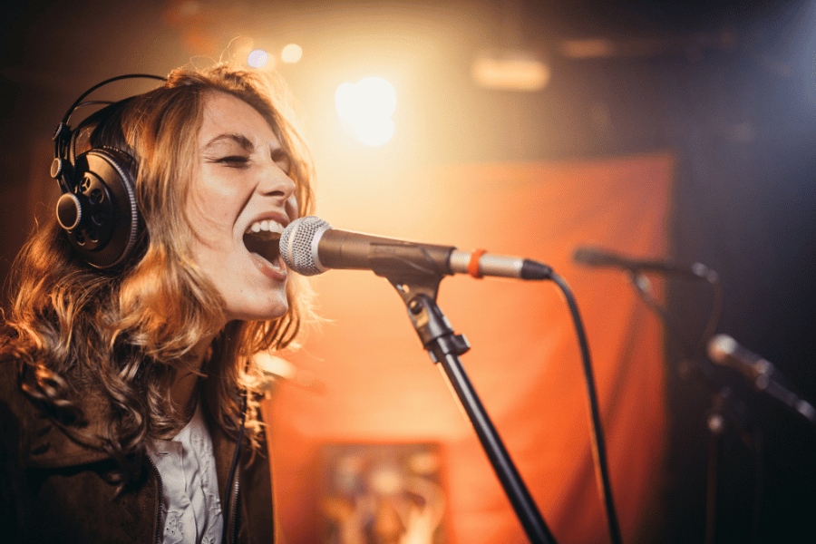 female singer with over ear headphones singing loudly into microphone