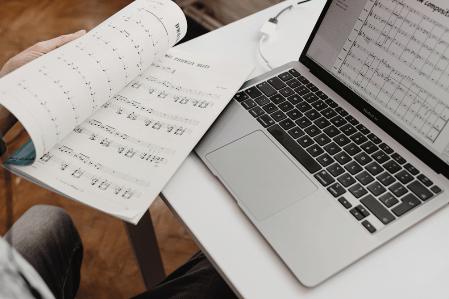 a person sitting at a computer with sheet music looking at music theory examples