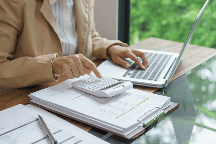 a woman in a tan blazer with a computer and calculator at a desk trying to figure out how much to charge for music lessons