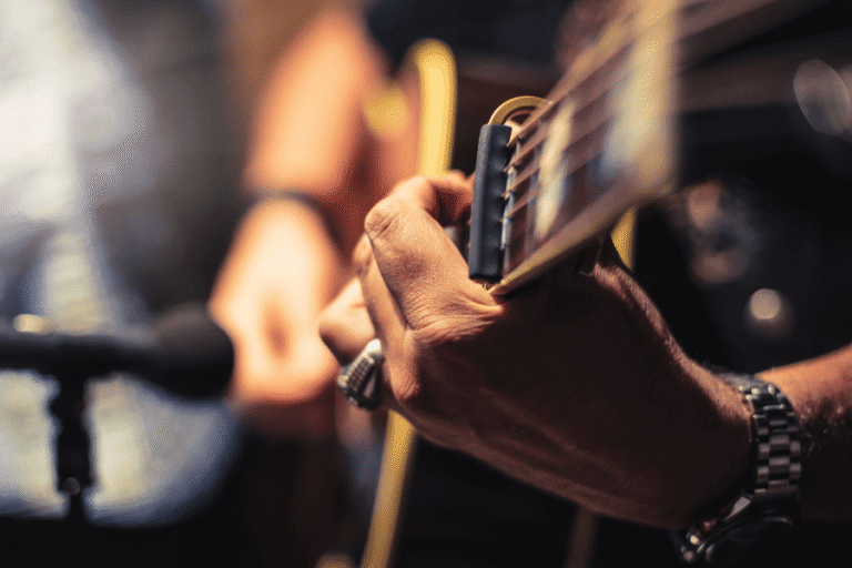 a closeup of a male playing acoustic guitar in front of an ambient microphone
